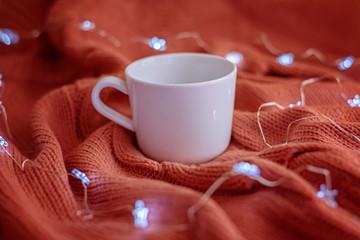 Wall Mural - Tea cup on warm knitted coral blanket and star lights. Mockup.