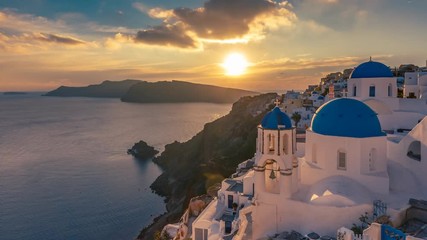 Fototapete - Beautiful view of Churches in Oia village, Santorini island in Greece at sunset, with dramatic sky. 4K day to night transition timelapse.