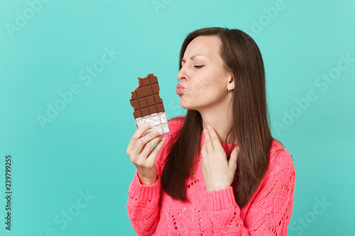Pretty Young Woman In Knitted Pink Sweater Blowing Sending Air Kiss To Chocolate Bar In Hands Isolated On Blue Turquoise Wall Background Studio Portrait People Lifestyle Concept Mock Up Copy Space