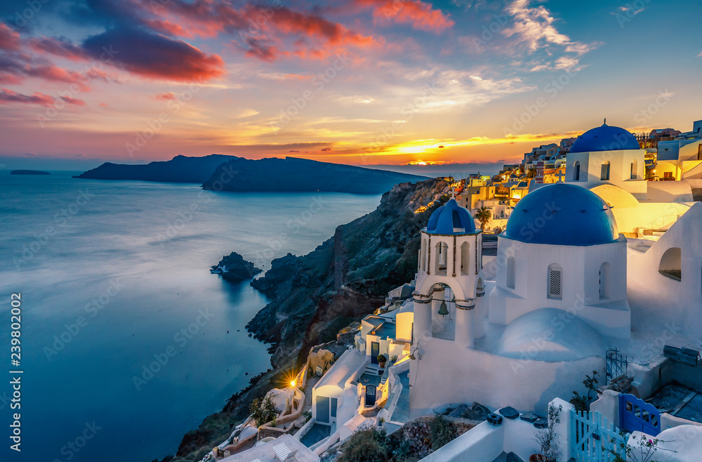 Beautiful view of Churches in Oia village, Santorini island in Greece at sunset, with dramatic sky. - obrazy, fototapety, plakaty 