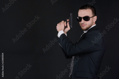 Man in black suit and sunglasses hold a gun in his hand Poster Mural XXL