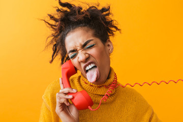 Poster - Portrait of joyous african american woman with afro hairstyle screaming and holding red handset, isolated over yellow background