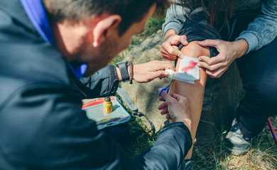 Young man healing knee to a young woman who has been injured doing trekking