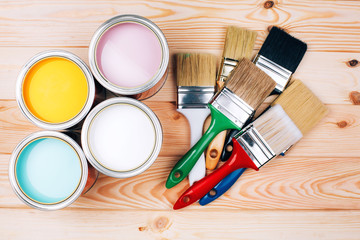 Four open cans of paint with brushes on natural wooden background. Yellow, white, pink, turquoise colors. Renovation concept.