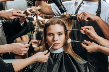 beautiful girl looking at camera while stylists applying makeup and doing hairstyle in beauty salon