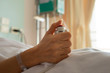 Hand holding  nurse call button,selective focused..Woman patient  in hospital dress under white blanket holding red emergency call button while lying in  bed.