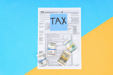 top view of tax form, money rolls and card with 'tax' word on blue and yellow background