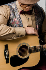 Wall Mural - close up view of young mixed race male musician in eyeglasses and hat posing with acoustic guitar isolated on black