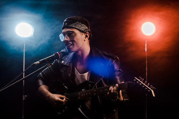 Wall Mural - smiling male musician singing in microphone and playing on electric guitar on stage during rock concert