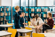 © LIGHTFIELD STUDIOS - young female librarian holding cup and looking at schoolkids reading books in library