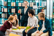© LIGHTFIELD STUDIOS - young female librarian holding cup and looking at smiling schoolkids in library