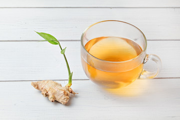 Wall Mural - Cup of freshly brewed amber tea, hot steam makes tiny wet drops on glass. Dry ginger root with green sprout next to it.