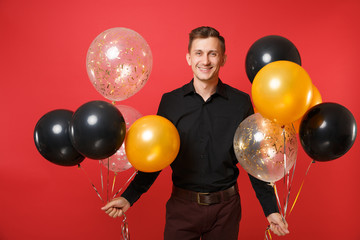 Smiling young man in black classic shirt holding air balloons celebrating isolated on bright red background. Valentine's International Women's Day Happy New Year birthday mockup holiday party concept.