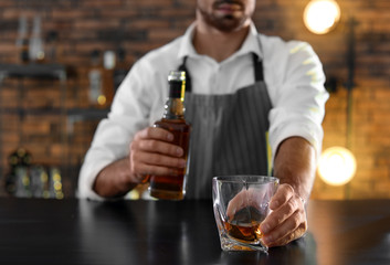 Poster - Bartender with glass and bottle of whiskey at counter in bar, closeup. Space for text