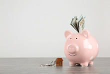 Piggy Bank With Dollar Banknotes And House Keys On Table Against White Background. Space For Text