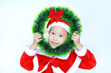 Wall Mural - Happy little child girl in Santa costume with holding Christmas round wreath on her face on white background. Merry Christmas and Happy New Year Concept.