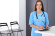 Doctor woman at work. Portrait of female physician filling up medical form while standing near reception desk at clinic or emergency hospital. Medicine and healthcare concept