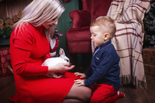 Beautiful Blonde Mother Showing To Son White Rabbit. Christmas Stocking Wood And Decorations On The Background. Concept Of Happy Christmas Holiday