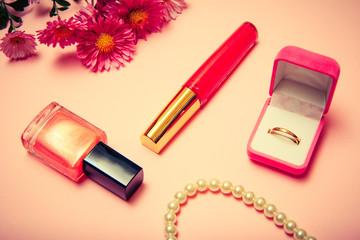 Box with golden ring, lipstick and flowers on a pink background,