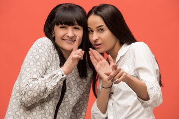 Wall Mural - A portrait of a surprised mother and daughter at studio on living coral background. Trendy colors. Human positive emotions and facial expressions concept