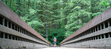Female Hiker Standing At End Of Bridge For Perspective