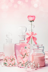 Wall Mural - Variety of cosmetic product bottles with roses essence standing on white pink background with bokeh. Skin care, cosmetic shop, sale and abstract beauty concept