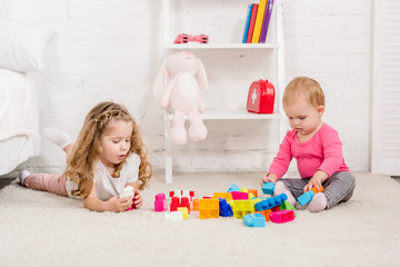 adorable sisters playing with constructor on carpet in children room