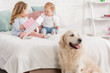 © LIGHTFIELD STUDIOS - adorable children playing on bed, golden retriever sitting near bed in children room