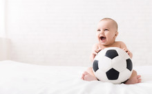 Newborn Baby Sitting With Soccer Ball On Bed