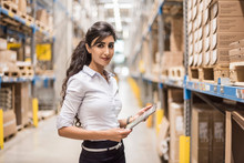 Portrait Of Young Woman With Black Hair Holding Digital Tablet In Factory Warehouse