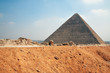 Pyramid of Gyza blue sky view with road and sand embankment - without tourists and Cairo, capital of Egypt, on background