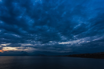 beautiful sunset cloudy sky and dark sea water with silhouettes of mountains in background. night is