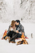 young couple on a date in the winter forest is heated by the fire and drink cocoa
