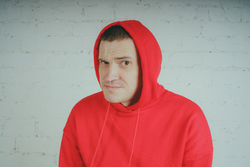 Wall Mural - Handsome guy posing by a brick wall. Crazy man in a red hoodie