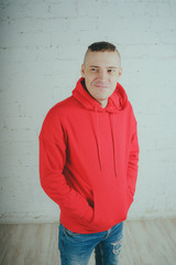 Wall Mural - Handsome guy posing by a brick wall. Crazy man in a red hoodie