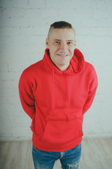 Wall Mural - Handsome guy posing by a brick wall. Crazy man in a red hoodie