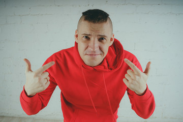 Wall Mural - Handsome guy posing by a brick wall. Crazy man in a red hoodie