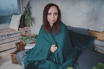 Portrait of positive cheerful girl sitting on sofa in comfortable apartment covered by plaid 