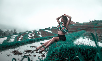 Beautiful young woman seat at typical Asian hillside with rice farming full of water, mountain shape green cascade rice field terraces paddies. Ubud, Bali, Indonesia. Tonned