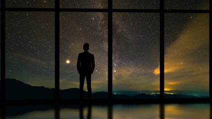 Wall Mural - The businessman standing near window on a starry sky background. time lapse