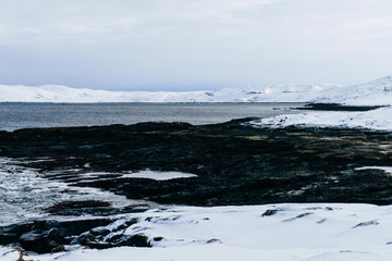 beautiful snow coast with sharp rocks and large stones of the cold blue sea in the north of the Arctic Circle