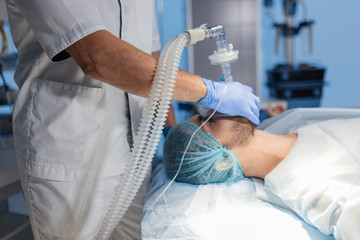 Wall Mural - Male assistants prepares a patient to invasive surgery in the Hospital operating room, holding oxygen mask over man s face, close up