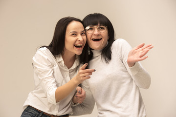 Wall Mural - A portrait of a happy mother and daughter at studio on gray background. Human positive emotions and facial expressions concept