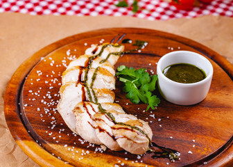 Wall Mural - Sliced grilled chicken breast with pesto sauce on wooden cutting board. Close up