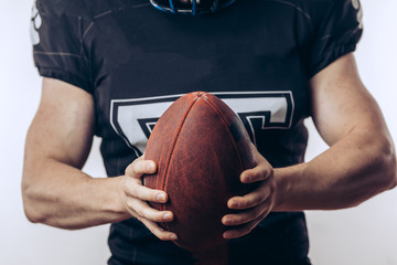 Wall Mural - Muscular american football player in uniform and helmet holding ball, ready to play and fight for win, isolated over white background.