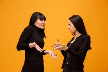 Wall Mural - A portrait of a unhappy mother and daughter at studio on gold background. Trendy colors. Human negative emotions and facial expressions concept