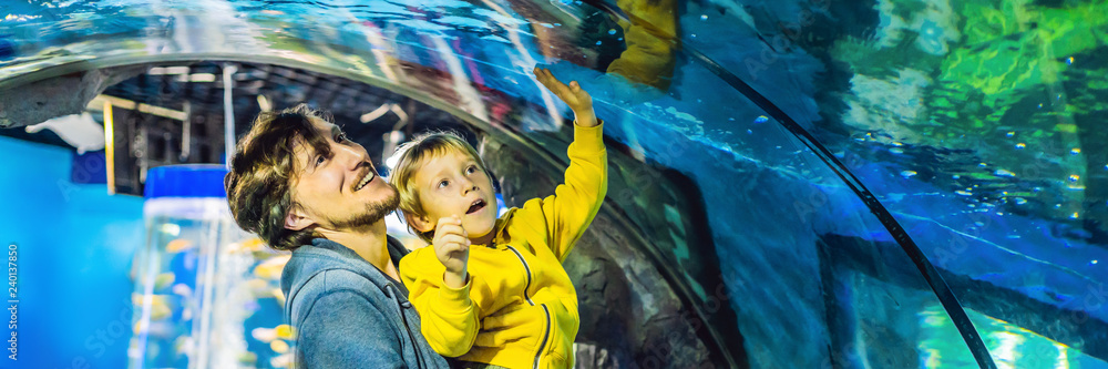 Obraz na płótnie Father and son look at the fish in the aquarium in oceanarium BANNER, LONG FORMAT w salonie