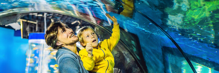 Wall Mural - Father and son look at the fish in the aquarium in oceanarium BANNER, LONG FORMAT