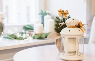 Decorative lantern of white color, white candles in the background.