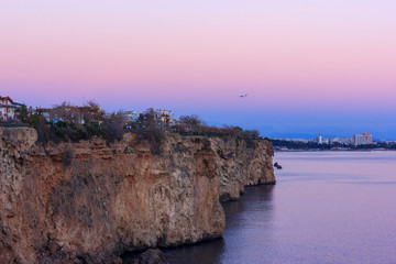 Wall Mural - Pink sunset over the Mediterranean Sea. Airplane in the sky over the rocks
